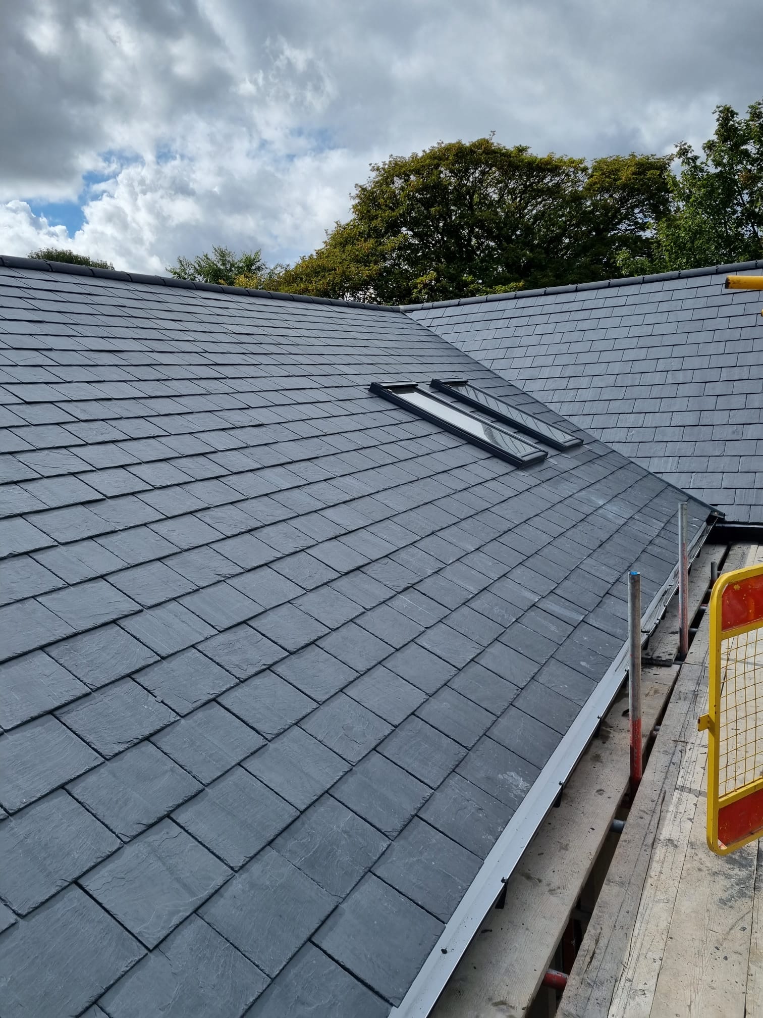New build residential property with a completed slate roof installation by C&J Construction & Roofing, featuring dark grey tiles, black fascias and integrated roof windows